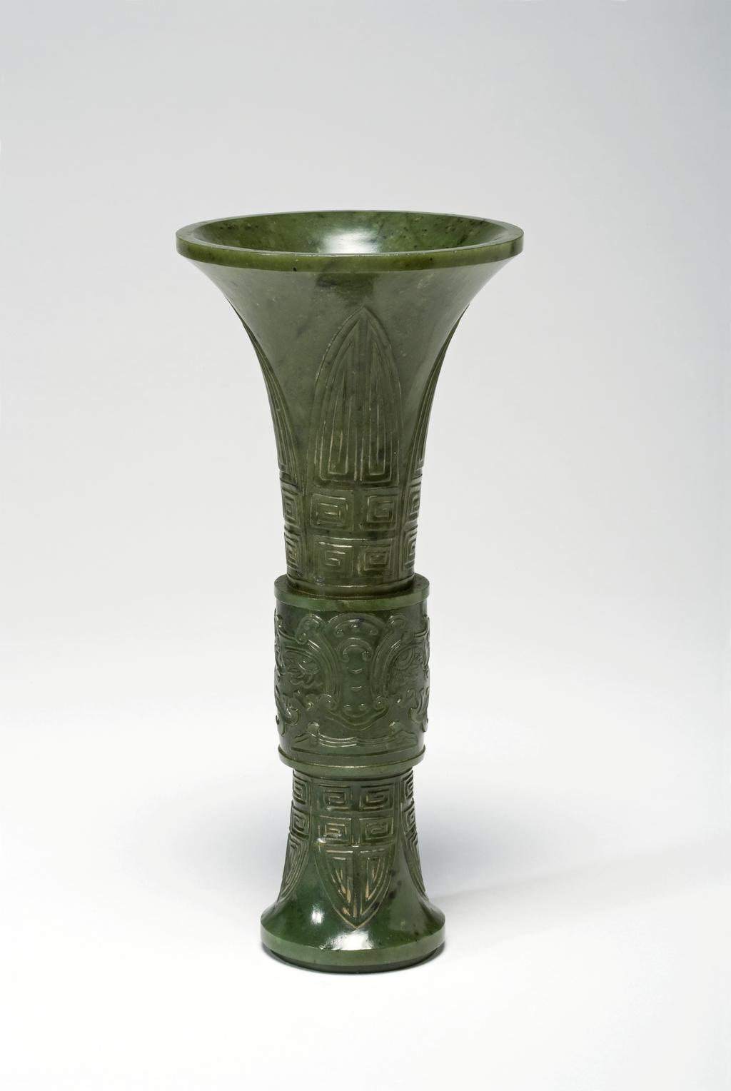 An image of Altar set of five pieces. Dark green with black spots; a Buddhist altar set of five pieces; two pricket candlesticks, two vases, and an incense burner. The two vases and incense burner are carved with ancient jade designs. The set are mounted on an elaborately carved wooden stand. Jasper, 1700-1800. Chinese.