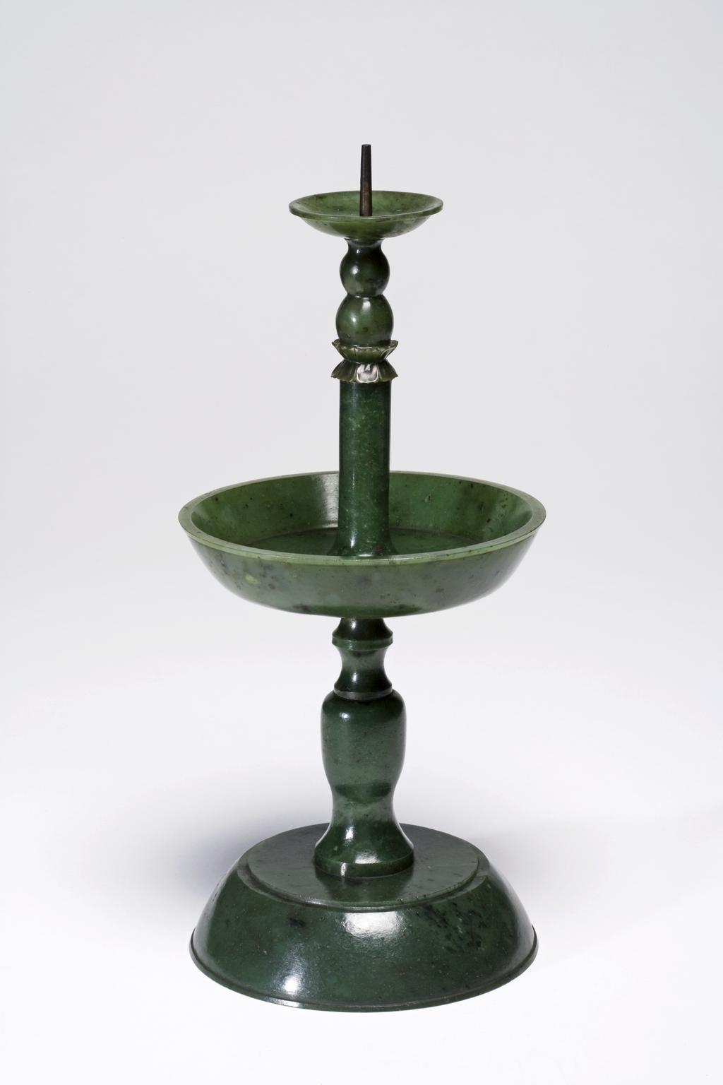 An image of Altar set of five pieces. Dark green with black spots; a Buddhist altar set of five pieces; two pricket candlesticks, two vases, and an incense burner. The two vases and incense burner are carved with ancient jade designs. The set are mounted on an elaborately carved wooden stand. Jasper, 1700-1800. Chinese.