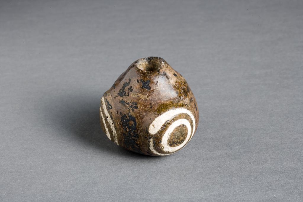 An image of GLASS BEADBead. Three-eyed. Brown glass, pebble-like, with white concentric circles at each of three corners.