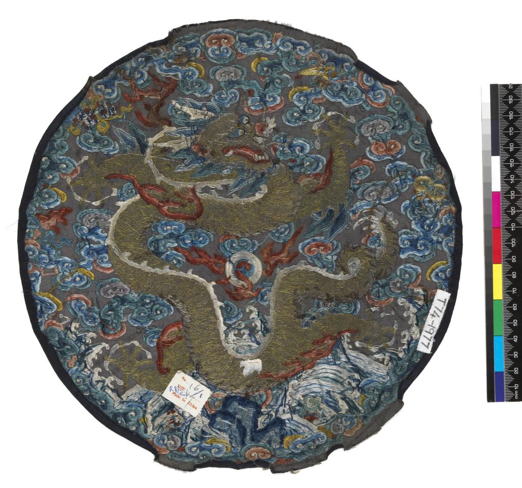 An image of Textiles. Roundel. Unknown maker, China. Five-clawed dragon on a background of waves and clouds, with six precious objects around perimeter. Silk and metal embroidery on satin; blue ground with polychrome embroidery - satin stitch, stem stitch, encroaching satin, seed stitch (Peking knot), with laid and couched work. Diameter, whole, 28 cm, circa 1750-circa 1775. Acquisition Credit: Given by Mrs. Soame Jenyns, in accordance with the wishes of her late husband, Soame Jenyns.
