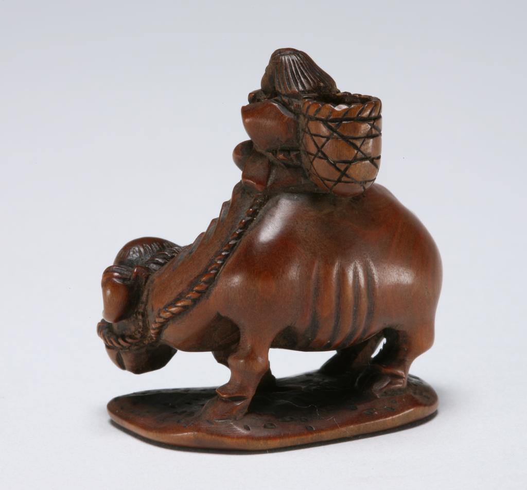 An image of Netsuke. A young attendant playing a flute on top of an ox. Unknown maker, Japan. Boxwood, carved, 1800-1850.