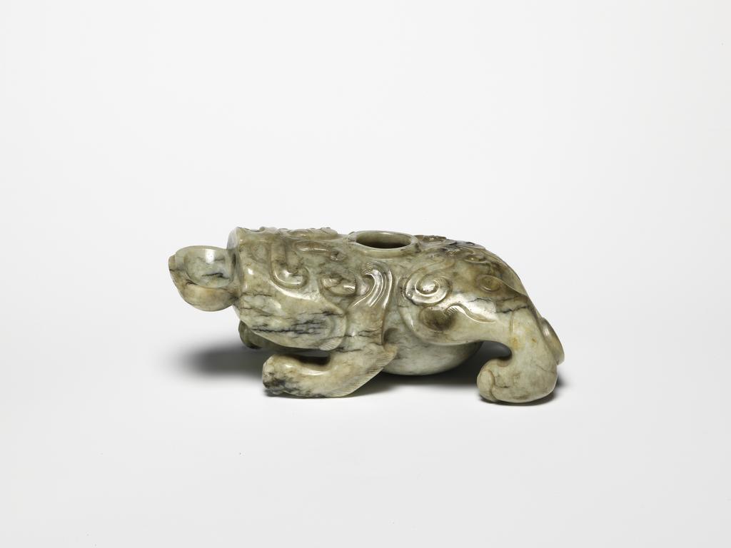 An image of Water Dropper. Unknown carver. Jade with areas of black, carved with mythical beast holding a shallow bowl. Wings extend from the four legs and a hole was drilled in the middle of its back. Jade, greyish, 1500-1600. Chinese. No dimensions recorded.