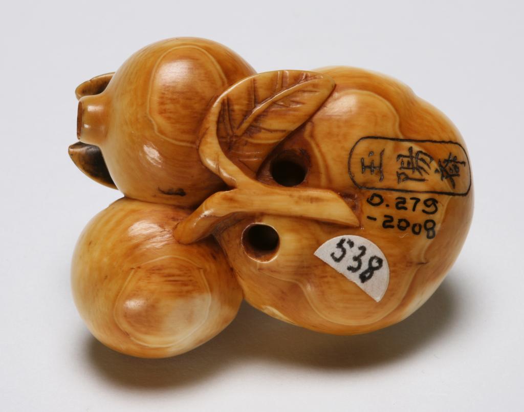 An image of Netsuke. Unknown maker, Japan. A large persimmon and two pomegranates on a twig, a cicada is perching on one of the pomegranate. There is a minute scale landscape inside the persimmon. Ivory, carved, 1830-1870.