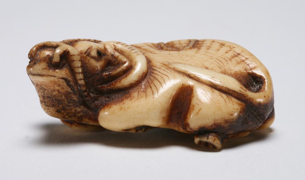 An image of Netsuke. Unknown maker, Japan. An ox reclining with its head turned to left, its eye are inlaid with horn. Stag antler, 1800-1850.