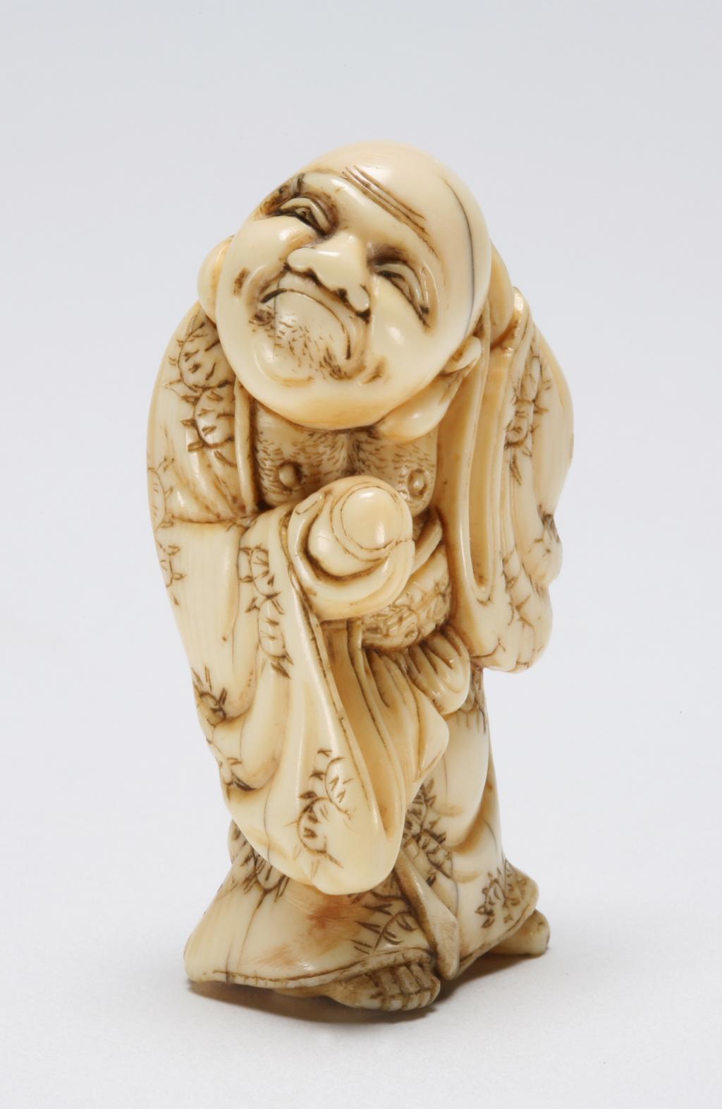 An image of Netsuke. Unknown maker, Japan. Hotei standing with his head turned to left and scratching the back of his head with his left hand while holding a Tama (jewel ball) in his right hand. Ivory, carved, 1770-1830.