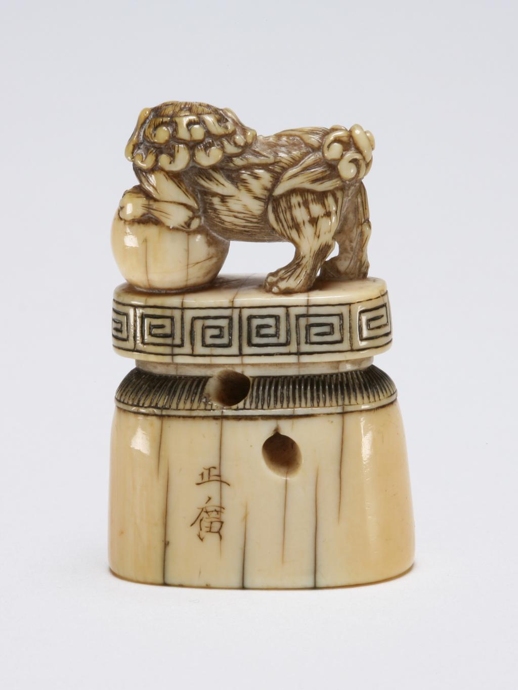 An image of Netsuke-Seal. Unknown maker, Japan. An oval shape seal with a carving of a Shishi standing with two paws on the jewel-ball. Ivory, carved, 1800-1850.