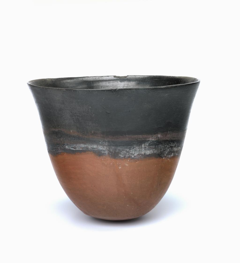 An image of Vessel. Clay beaker, with black top decoration. Production Place: Egypt, Nubia (Southern Egypt/Sudan). Find Spot: Abydos Egypt; grave 4. Kerma beaker, with black top decoration. The vessel is made from Nile Silt clay and has very thin walls, measuring from 2-5 mm in thickness. The rim is asymmetrical and the interior was smoothed with fingers, and burnished (rubbed with a hard object horizontally). Outside there is a red wash on the lower section of the pot which was then polished. This type of ware is called red and black. This vessel came from the grave of a Nubian living in Egypt who belonged to a group of people called the Kerma culture. Only a few familes of the Kerma people found their way into Egypt. It is therefore of interest that they brought pottery with them, along with other goods, but chose a traditional Egyptian manner of burial. The base is rounded. The pot is complete, which is remarkable given its fragile structure. Clay, handmade, burnished and polished, diameter 14.2 cm, height, 11.7, cm, ca 1785-1650 BC. Thirteenth Dynasty; Middle Kingdom; Second Intermediate period.