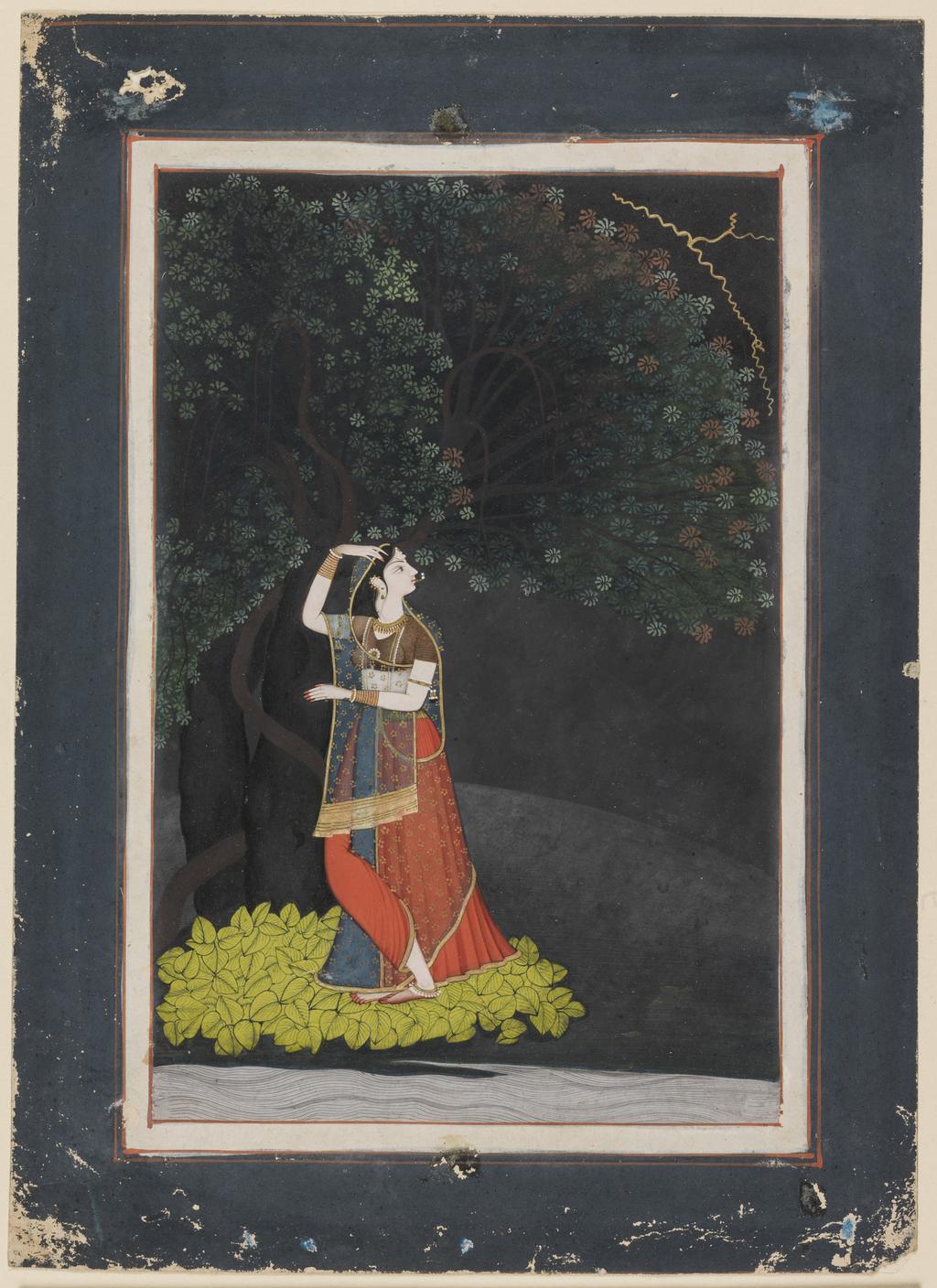 An image of Miniature. A lady (Radha) waiting for her lover, standing upon a bed of leaves, under a tree on night of storm. Unknown miniaturist. Watercolour, bodycolour including white, pen and ink with gold on paper, height 211 mm, width 139 mm, circa 1790. Pahari. Acquisition Credit: Bequeathed by P.C. Manuk and Miss G.M. Coles in 1946 through the National Art Collections Fund.