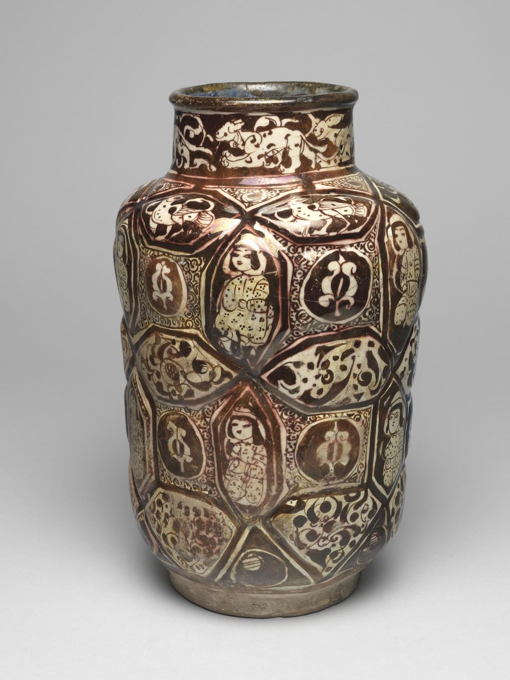 An image of Jar. Islamic pottery. Lustre ware. Unknown, probably Kashan. Shape: cylindrical jar with lobbed body, straight neck and a bead rim. Sits on a thick, wide foot ring. Exterior: rim is painted with lustre. On the neck a hunt scene of running quadrupeds, including hares and dogs, is reserved on a lustred ground that also contains fleshy palmettes. On the body lozenge or rectangular shape moulded lobes are filled with a geometrical pattern of seated figures, birds or palmettes, all of which are reserved in lustre; these alternate with arabesques painted in lustre. Spandrels around the palmettes and on the shoulder are filled with lustre scrolls. Interior: lustre paint continues on the rim. The remainder of the vessel is covered with a blue glaze that is painted with a pseudo inscription in lustre on the neck. Fritware, mould made, coated in a white glaze painted in lustre. Height, whole, 30.6 cm, width, whole, 19.1 cm, diameter, rim, 10.7 cm, diameter, base, 12 cm, weight, whole, 1634 g, circa 1170- circa 1200. Seljuk Period.