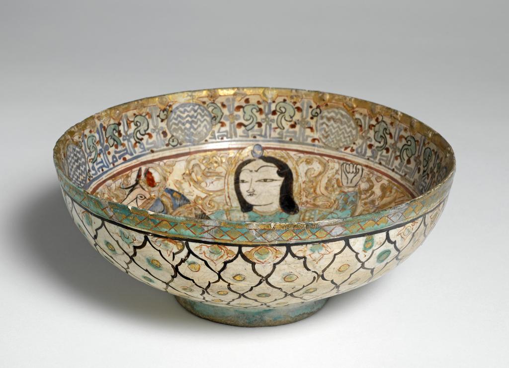 An image of Bowl. Buff fritware, wheel thrown, coated in an opaque white, crazed glaze with slip to create relief effect. Painted in the glaze in blue, turquoise and purple and red, black with gold leaf gilding over the glaze. Height 9 cm, width 21 cm, diameter (rim) 21 cm, diameter (base) 8.8 cm, circa 1175-1220. Seljuk, Minai.