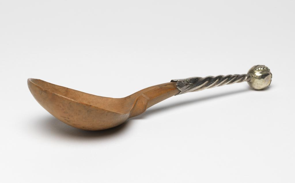 An image of Cutlery, flatware. Spoon. Unknown silversmith, Germany. Unknown woodworker, Germany. The wood bowl is a fig-shaped on a tapering stem which has been incised with two pairs of lines on the front. The silver handle is embossed with tapering spiral flutes and terminates in a silver-gilt pomegranate, which is capped with a quatrefoil (one petal missing). The stem and back of the pomegrate are scratch engraved 'MK' and 'RK' respectively. The wood bowl and tapering stem were carved. The silver handle was embossed and the seam down the back was soldered. The pomogranate was gilded and soldered to the silver handle. The hollow silver handle was glued over the short wood stem. The initials were engraved. Fruit wood, silver and silver-gilt, length, overall, 15.3, cm, 1650-1700. Production Note: the silver is not stamped with a maker's mark or any other identifying marks.
