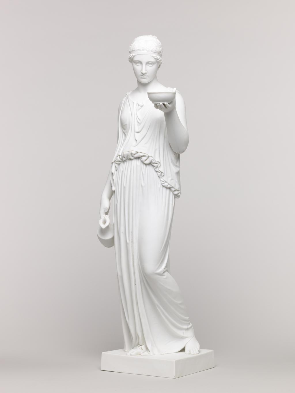 An image of Figure. Unknown lady. Standing figure, classical dress, holding bowl in left hand and jug in right hand. Royal Copenhagen Porcelain Factory, possibly, Denmark, Copenhagen. Parian (porcelain), slip-cast, height, 48 cm, length, 16.5 cm, width, 14 cm, length, base, 12.2 cm, width, base, 11.4 cm. Acquisition Credit: Accepted by H. M. Government in lieu of Inheritance Tax from the estate of G. D. V. Glynn, and allocated to the Fitzwilliam Museum.