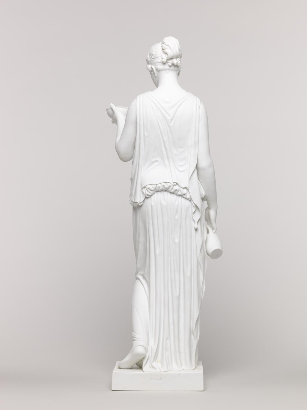 An image of Figure. Unknown lady. Standing figure, classical dress, holding bowl in left hand and jug in right hand. Royal Copenhagen Porcelain Factory, possibly, Denmark, Copenhagen. Parian (porcelain), slip-cast, height, 48 cm, length, 16.5 cm, width, 14 cm, length, base, 12.2 cm, width, base, 11.4 cm. Acquisition Credit: Accepted by H. M. Government in lieu of Inheritance Tax from the estate of G. D. V. Glynn, and allocated to the Fitzwilliam Museum.
