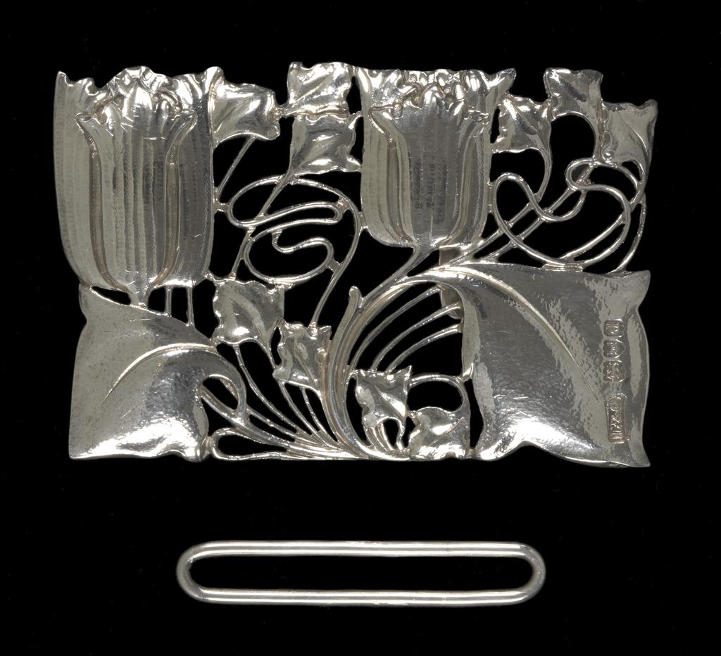 An image of Jewellery. Waist clasp. Knox, Archibald (British, 1864-1933). Rectangular with a sinuous design of two tulips and foliage. On the back, a flattened hook and a bar to hold one end of the belt. Separate rectangular loop for the other end of the belt. Cast silver openwork, height, whole, 5.1 cm, width, whole, 7.9 cm, circa 1899-1900. Acquisition Credit: Given by Mrs J. Hull Grundy.