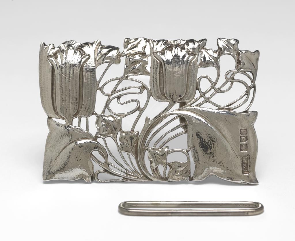 An image of Jewellery. Waist clasp. Knox, Archibald (British, 1864-1933). Rectangular with a sinuous design of two tulips and foliage. On the back, a flattened hook and a bar to hold one end of the belt. Separate rectangular loop for the other end of the belt. Cast silver openwork, height, whole, 5.1 cm, width, whole, 7.9 cm, circa 1899-1900. Acquisition Credit: Given by Mrs J. Hull Grundy.