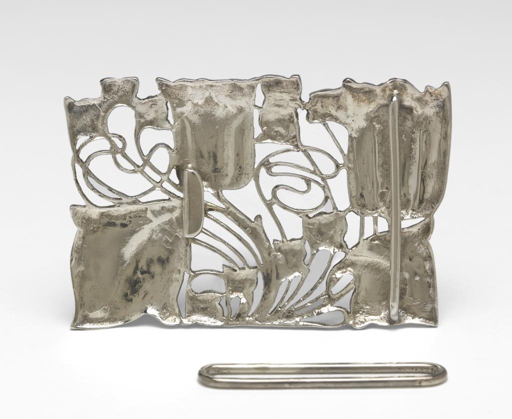 An image of Jewellery. Waist clasp. Knox, Archibald (British, 1864-1933). Rectangular with a sinuous design of two tulips and foliage. On the back, a flattened hook and a bar to hold one end of the belt. Separate rectangular loop for the other end of the belt. Cast silver openwork, height, whole, 5.1 cm, width, whole, 7.9 cm, circa 1899-1900. Acquisition Credit: Given by Mrs J. Hull Grundy.