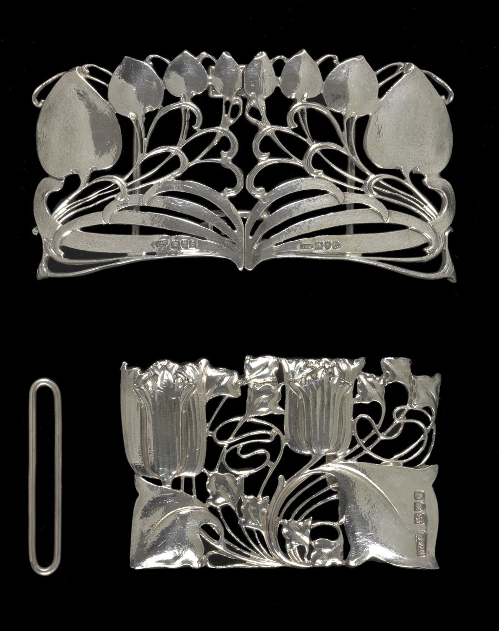 An image of Jewellery. Waist clasp. Knox, Archibald (British, 1864-1933). Rectangular with a sinuous design of two tulips and foliage. On the back, a flattened hook and a bar to hold one end of the belt. Separate rectangular loop for the other end of the belt. Cast silver openwork, height, whole, 5.1 cm, width, whole, 7.9 cm, circa 1899-1900. Acquisition Credit: Given by Mrs J. Hull Grundy.