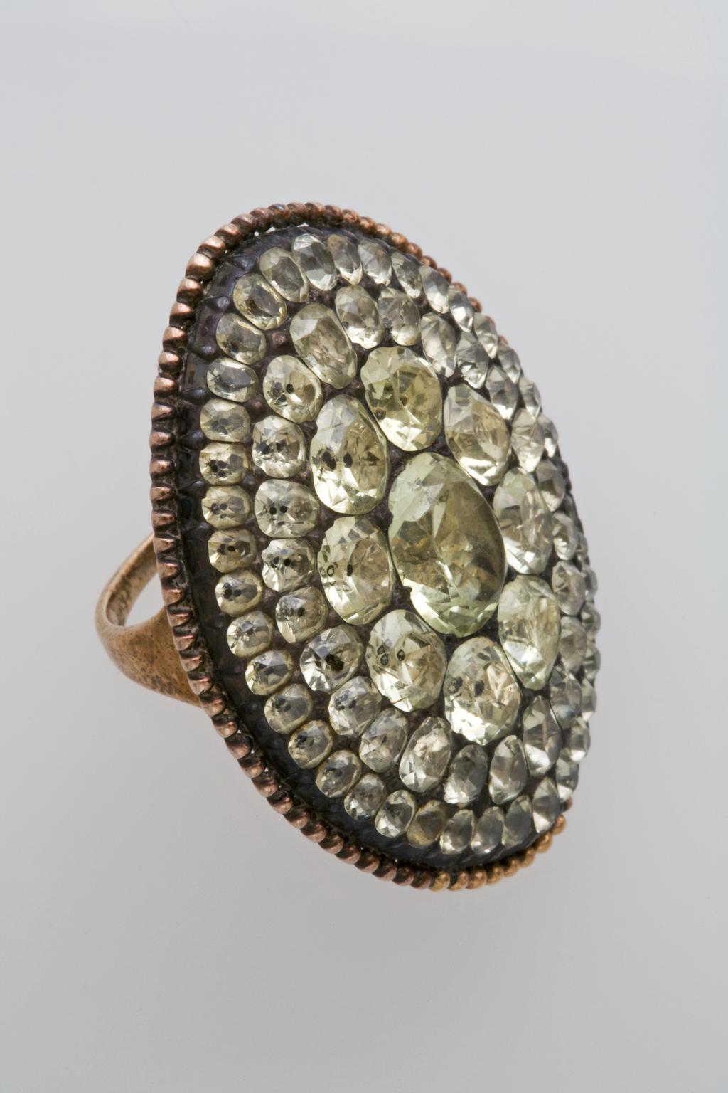 An image of Jewellery/Ring. Reddish-gold, the broad, almond-shaped bezel pavé set in silver with very pale yellow chrysoberyls. Diameter (hoop) 2 cm, length (bezel) 3.8 cm, width (bezel) 3 cm, circa 1770-1800. Notes: Accessioned as Spanish but may be Portuguese. 