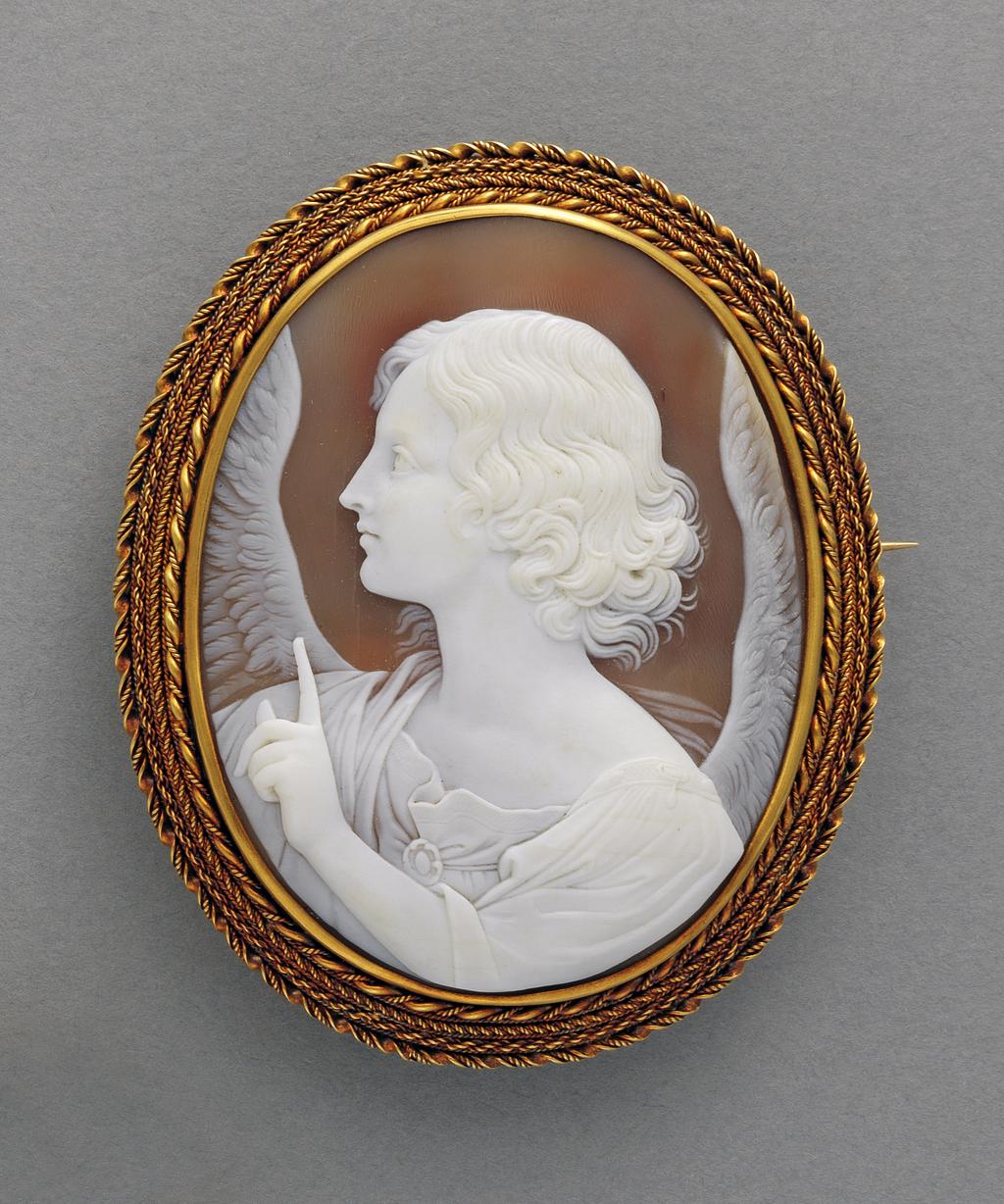 An image of Jewellery. Brooch. Shell cameo mounted in gold. Watherston & Brogden, England. Cameo bust of an angel in profile to the left with the index finger of its left hand raised, mounted in gold and surrounded by a border of four strands of gold ropework; pin-fastening across the back. In original red leather case (A), the lid of which is lined with white silk, printed in blue with the maker's name and adress: 'PARIS FIRST CLASS & LONDON PRIZE MEDALS/Watherston & Brogden/ Goldsmiths/ MANUFACTORY/16 Henrietta St/Covent Garden.WC/LONDON'. Gold, shell, height 7.21 cm, width 5.9 cm, 1862-1864. Victorian. Acquisition Credit: Given by Mrs J. Hull Grundy.