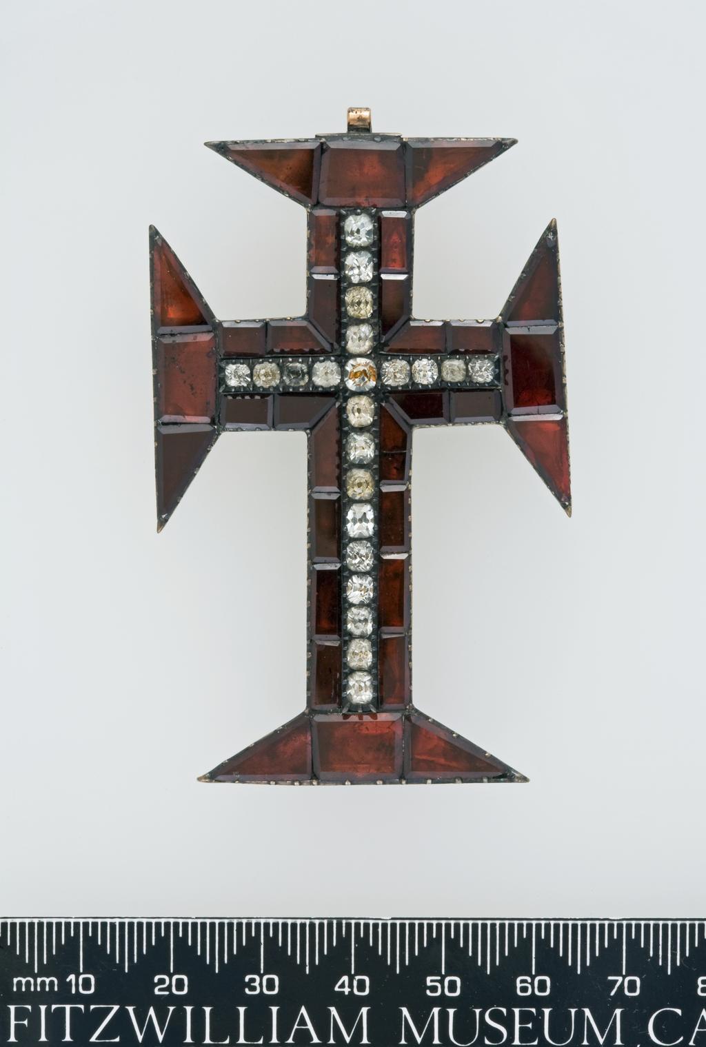 An image of Jewellery. Cross Pendant. Silver with closed back, set with table-cut garnets, surrounding a central cross of facetted crystals. Production Place: Portugal. Height (whole) 7.4 cm, width (whole) 4.4 cm, late 18th Century. Notes: The brooch from which the cross was suspended is missing. Accessioned as Spanish.