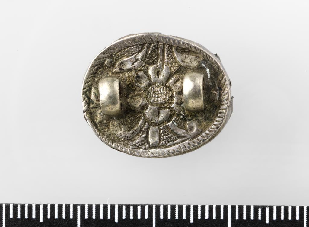 An image of Stamp seal. Cabochon ringstone, with 2 magi flanking a fire altar, mounted in silver brooch, with floral relief on back. Find Spot: Shiraz and Hamadan Iran. Depth 0.007 m, length 0.019 m, width 0.014 m, circa 501-600. Sasanian.